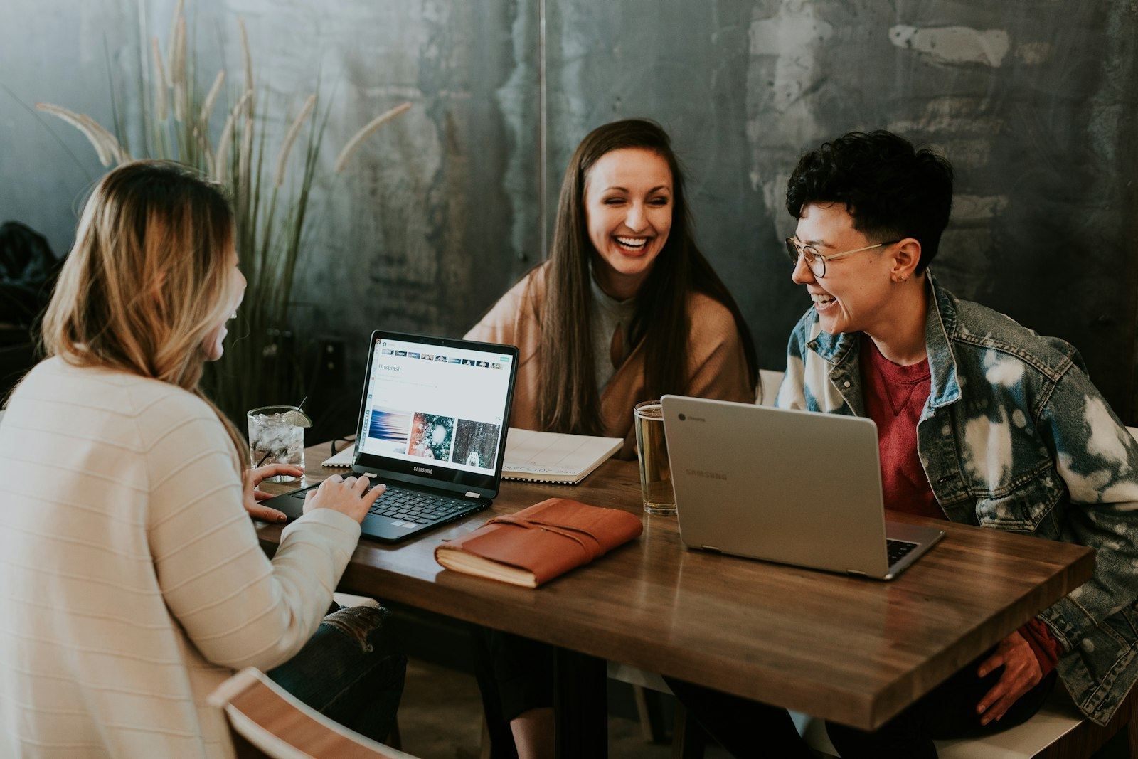Three students at a table with laptops, laughing