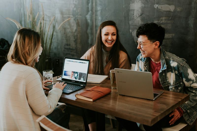 Three students at a table with laptops, laughing