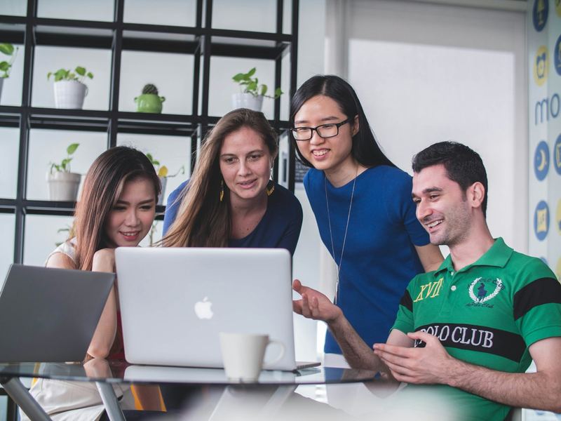 Four people around a laptop, one pointing at the screen